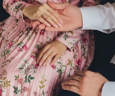 Close-up of a man's hands gently holding a woman's hands over her beautiful floral pink dress, representing courtship and things that destroy a marriage when proper care isn't taken.