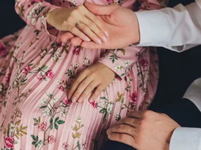 Close-up of a man's hands gently holding a woman's hands over her beautiful floral pink dress, representing courtship and things that destroy a marriage when proper care isn't taken.
