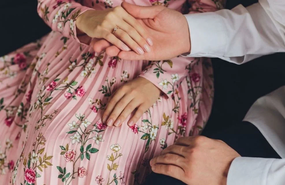 Close-up of a man's hands gently holding a woman's hands over her beautiful floral pink dress, representing courtship and things that destroy a marriage when proper care isn't taken.
