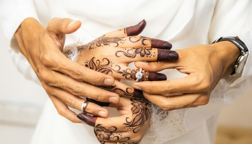 Hands with henna exchanging wedding rings, symbolising questions to ask before marriage in Islam
